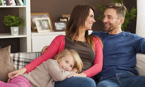 Smiling couple staring at each other on couch with young daughter.