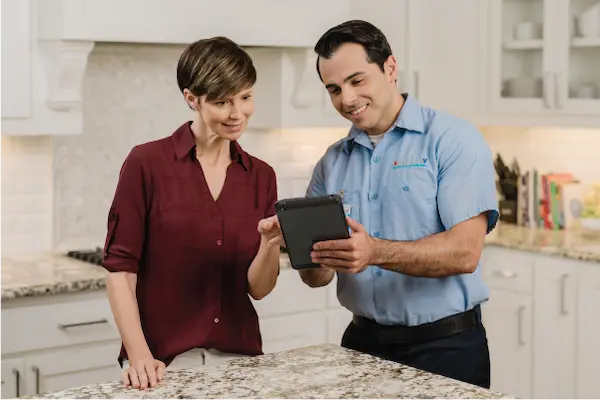 Aire Serv technician holding tablet device beside customer in modern residential kitchen with marble countertops.